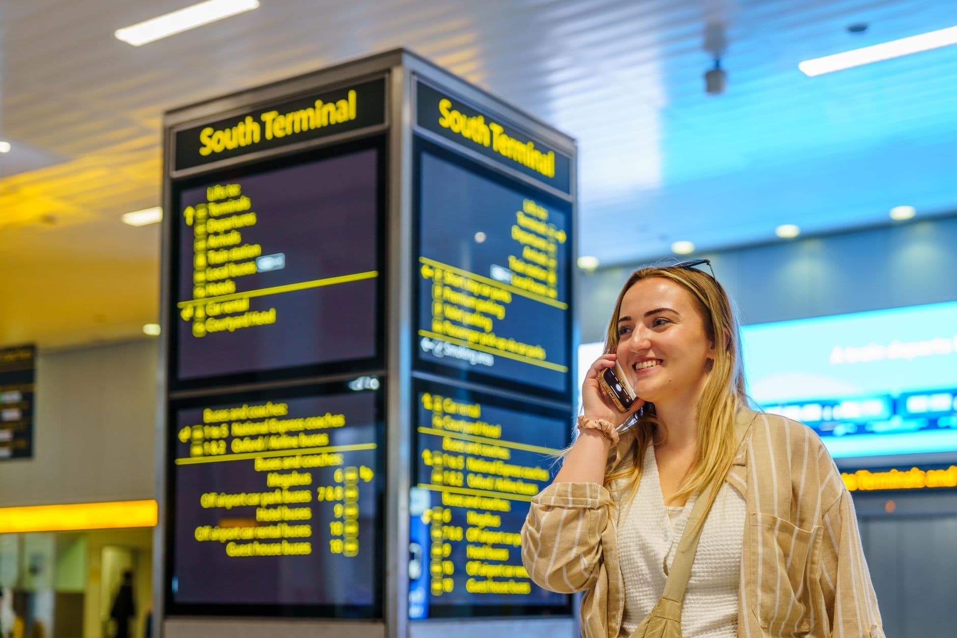 A person looking at their phone in a busy airport departure lounge, with luggage nearby, preparing for their flight.