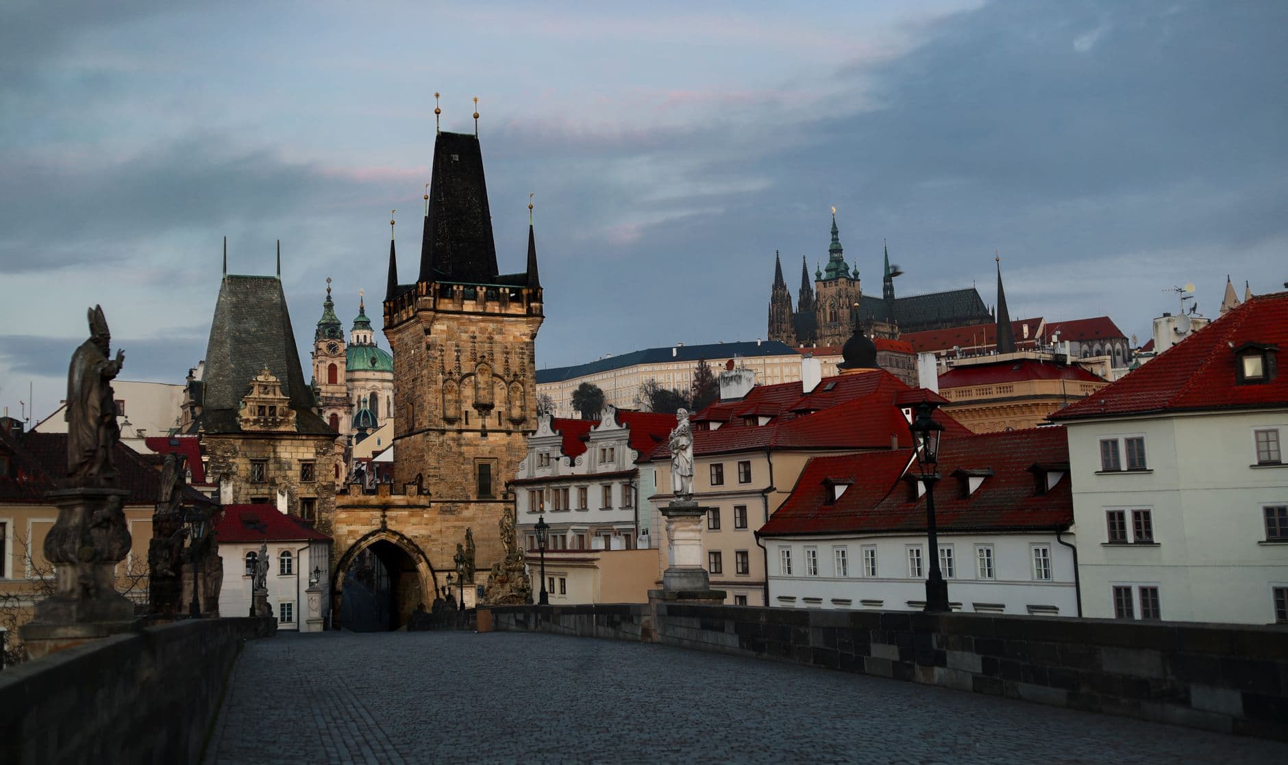Sunrise over Charles Bridge in Prague, Czechia, with the castle in the background and a few early morning strollers enjoying the quiet.