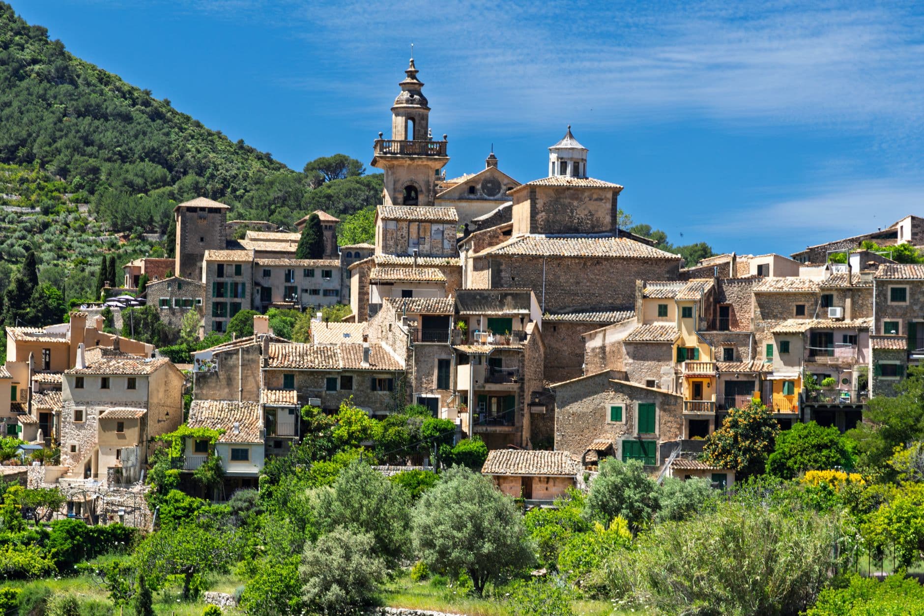 Ein idyllisches Bergdorf in der Serra de Tramuntana auf Mallorca, umgeben von grünen Hügeln und Zypressen.