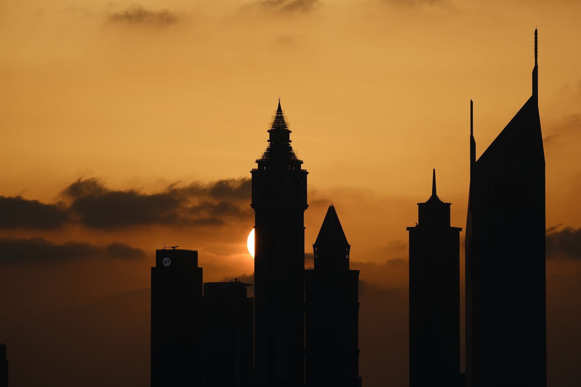 A panoramic view of the Dubai cityscape at sunset, with modern skyscrapers, a clear sky, and reflections on the water.