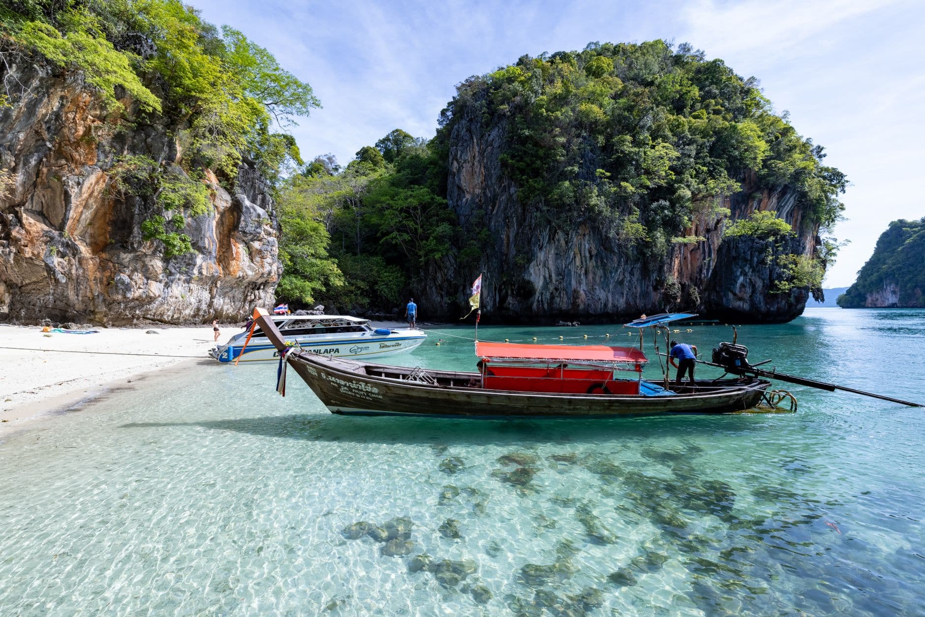 A traditional longtail boat on a turquoise sea, with lush green islands and clear skies in the background of Thailand.
