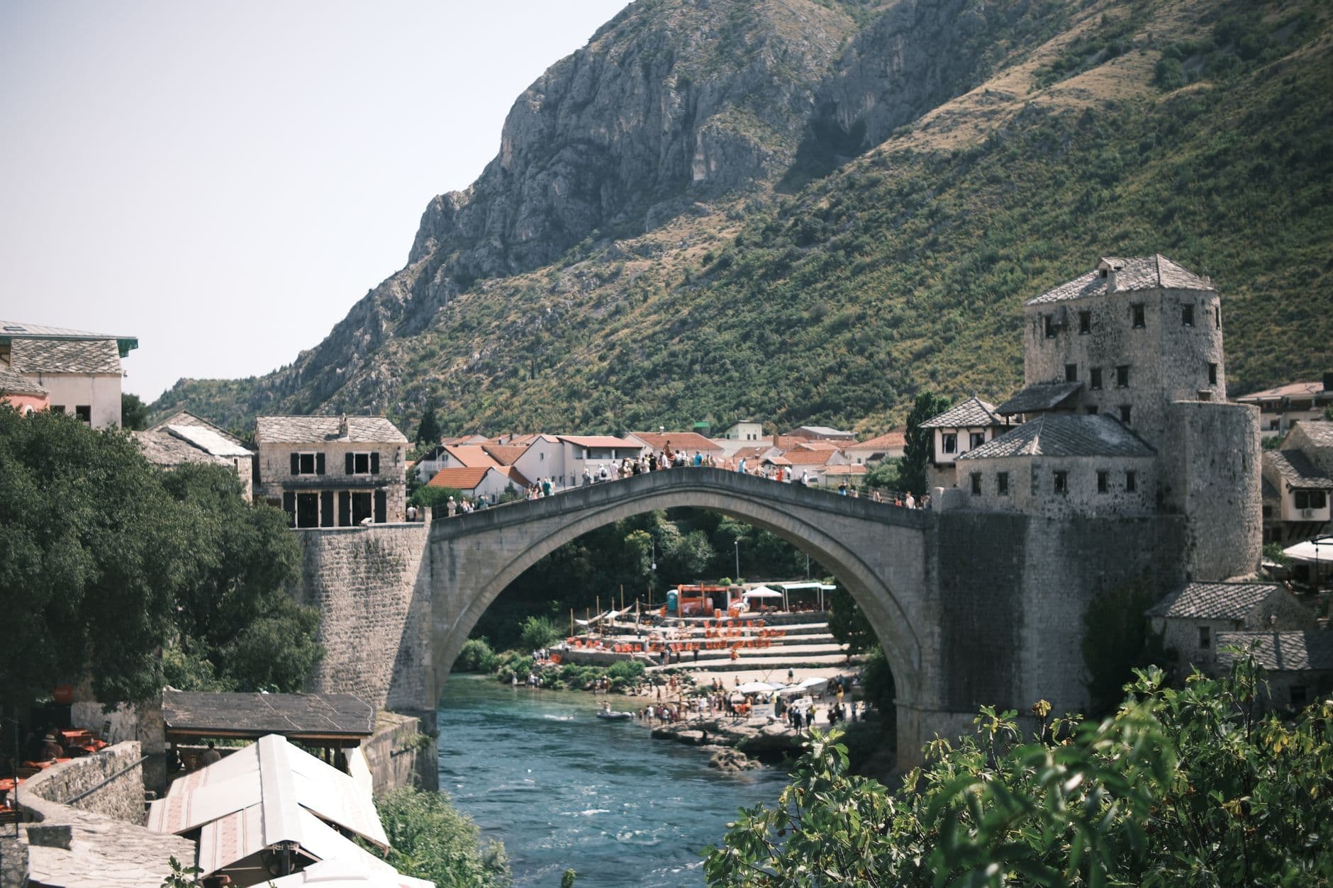The iconic Stari Most bridge in Mostar, Bosnia and Herzegovina, arching gracefully over the turquoise Neretva River, with historic Ottoman-era buildings lining the banks under a clear sky.