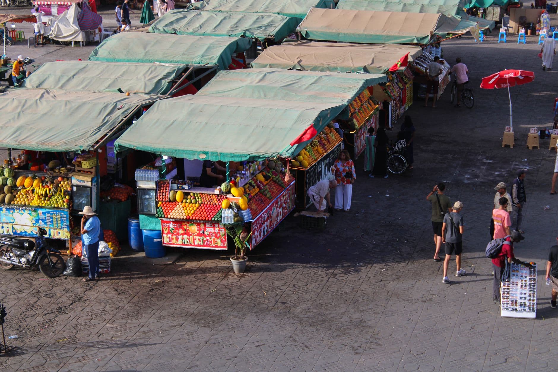 A vibrant, bustling scene in the Marrakech souks with colorful textiles, lamps, and people shopping, featuring a mix of shadows and bright light.