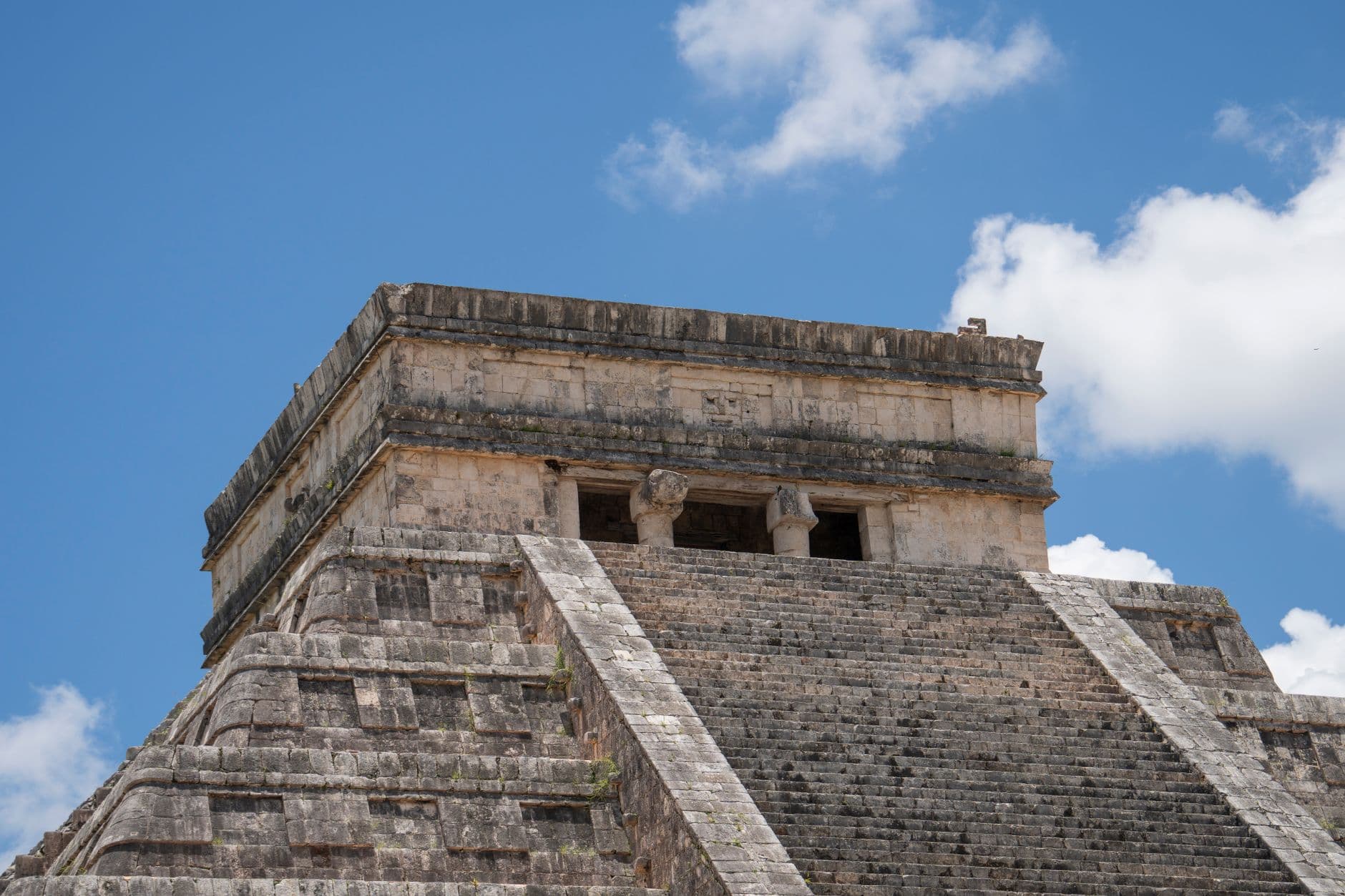 Ancient Mayan ruins of Chichen Itza under a clear sky in Mexico, with tourists exploring the site.