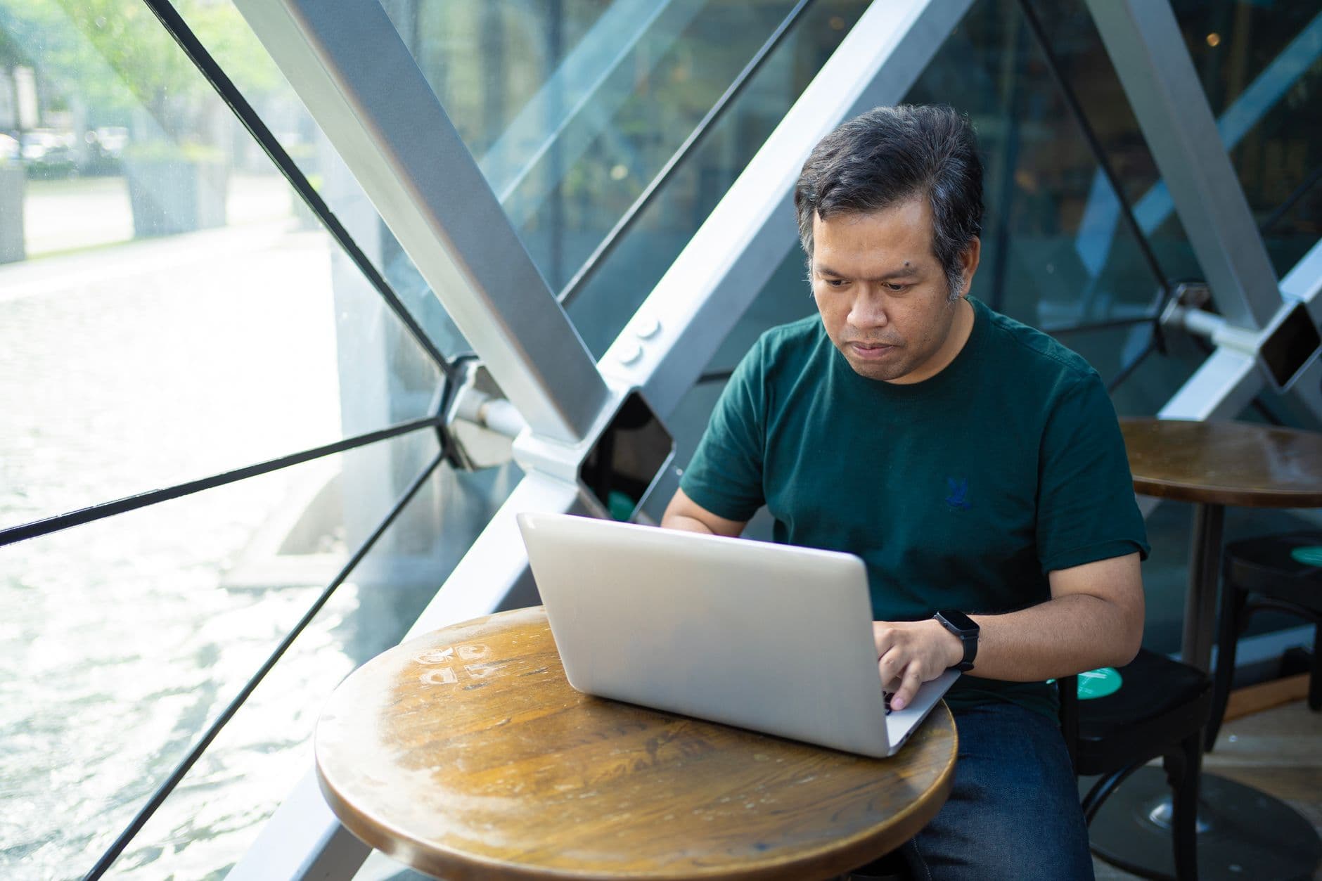 A person working on a laptop at a modern coworking cafe in Bangkok, with a smoothie and notebook on the table.