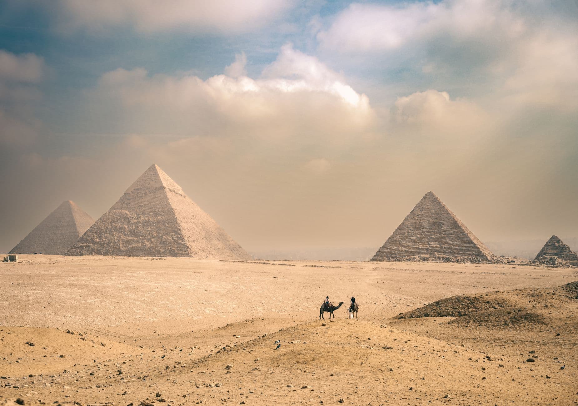 A traveler riding a camel with the Great Pyramids of Giza in the background under a clear blue sky, showing ancient wonders and modern travel.