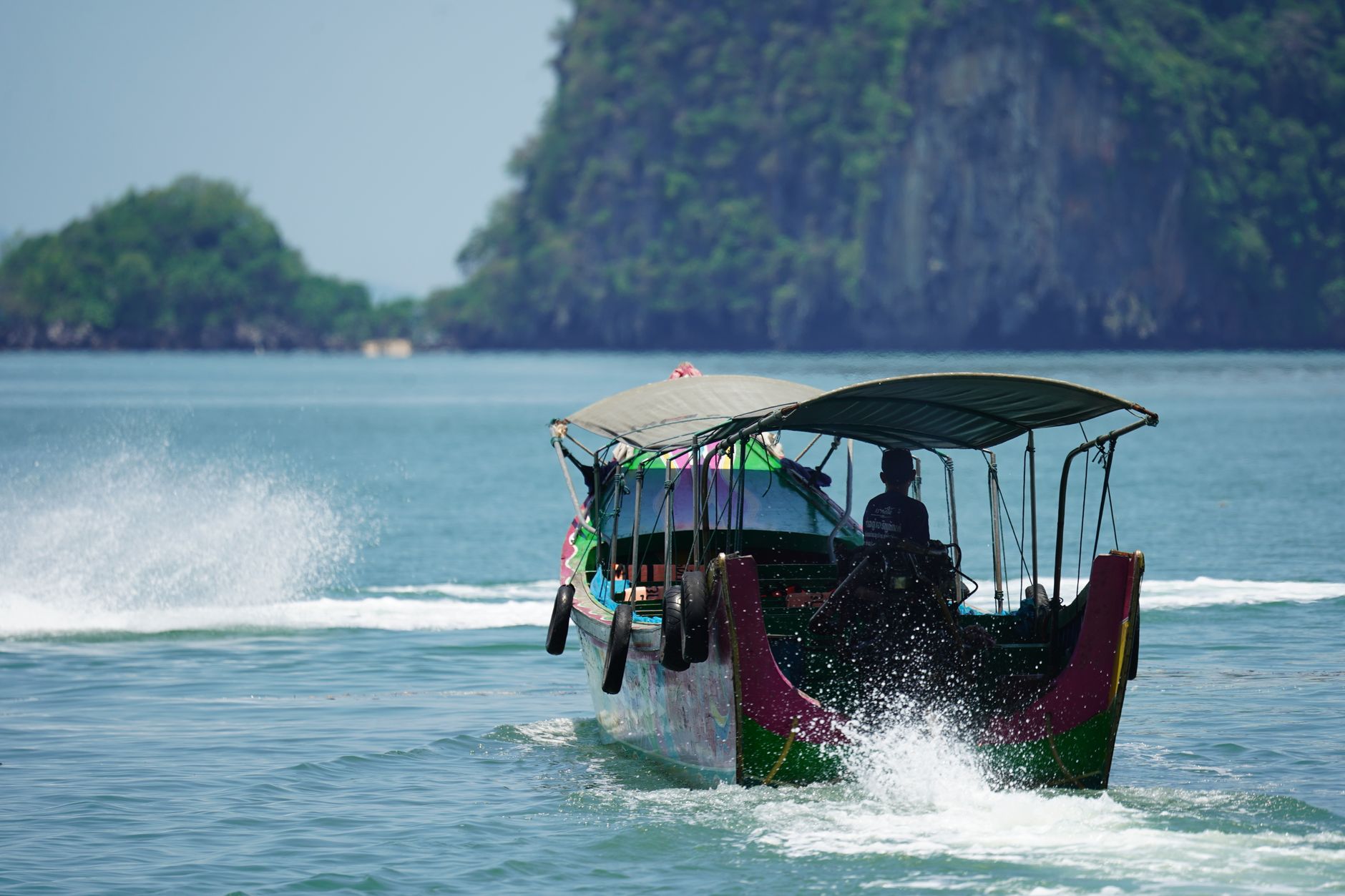 Ein traditionelles Longtail-Boot vor einer felsigen Insel in Thailand, bereit für Inselhopping.