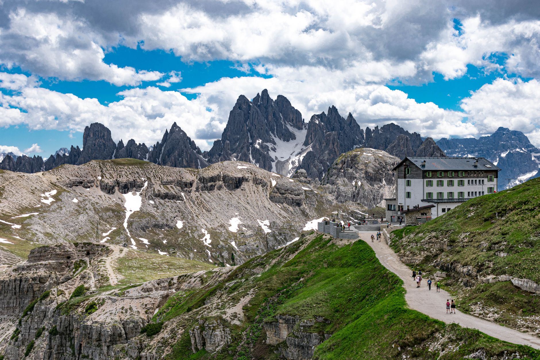 A traditional mountain hut, or rifugio, nestled in a green valley of the Dolomites with imposing peaks in the background.