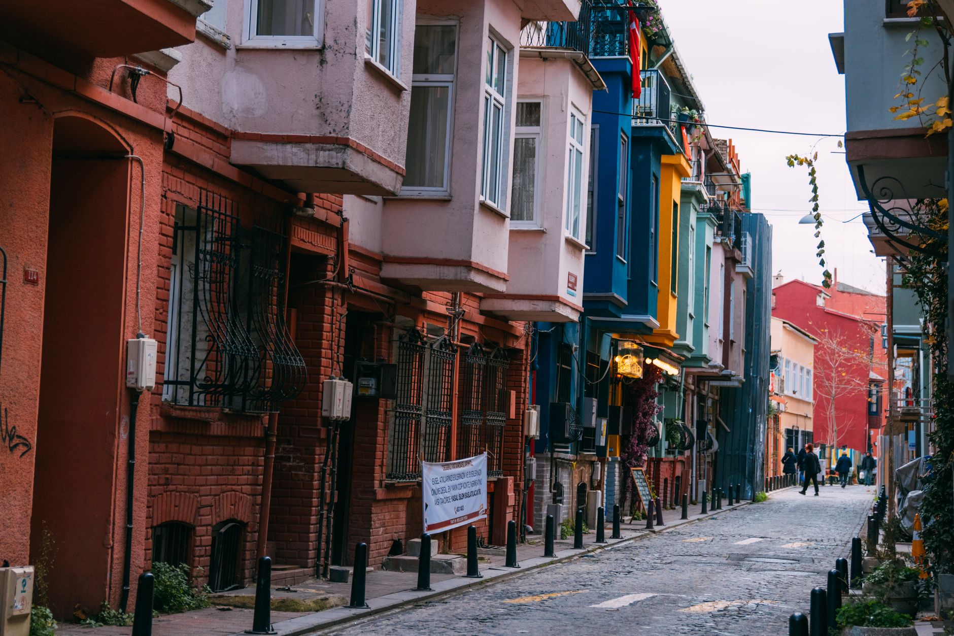 A narrow, cobbled street in Balat, Istanbul, lined with brightly painted historic houses in various shades of red, blue, and yellow.