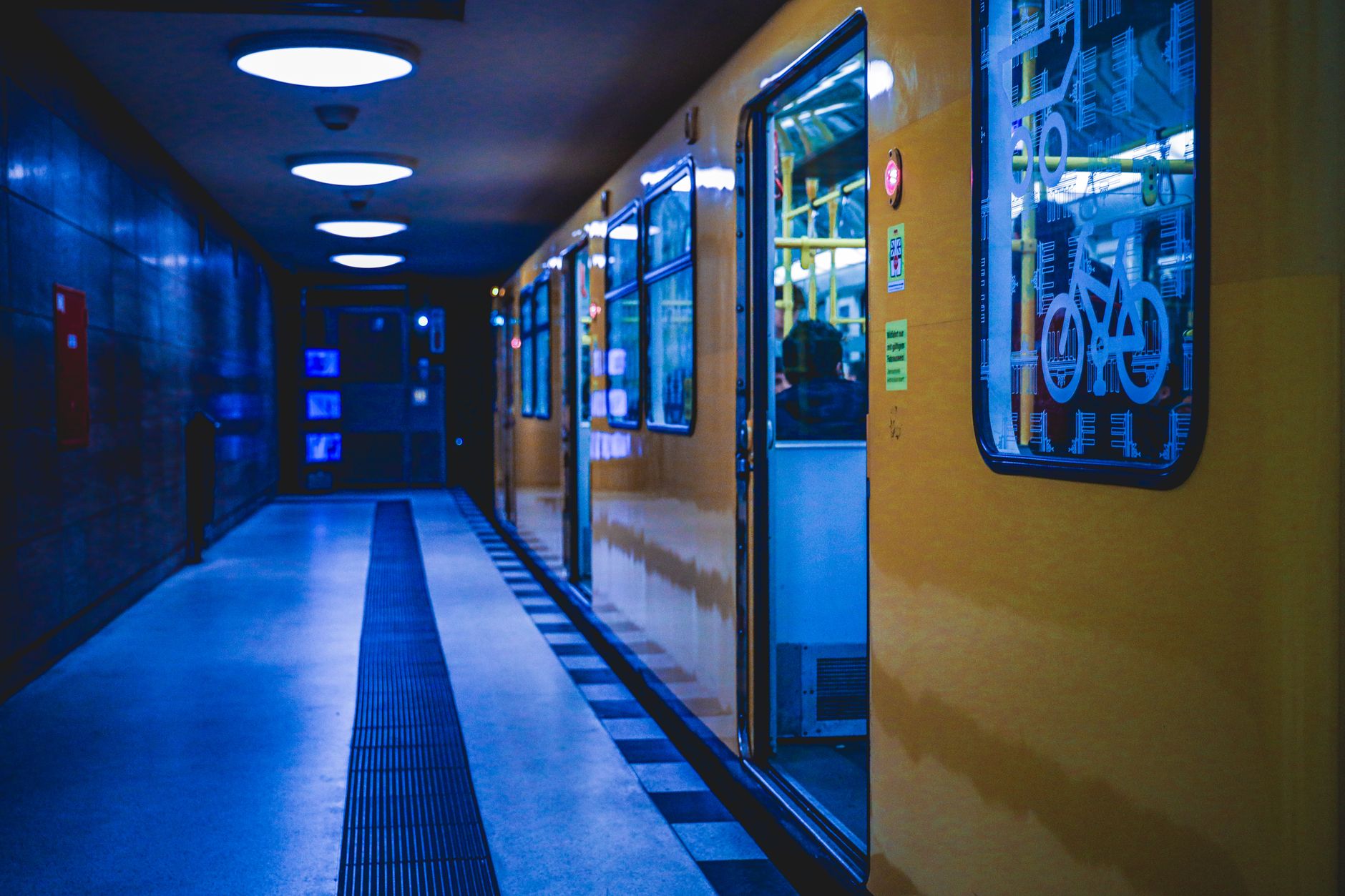 A U-Bahn train arriving at a brightly lit station in Berlin late at night, with a few passengers waiting.