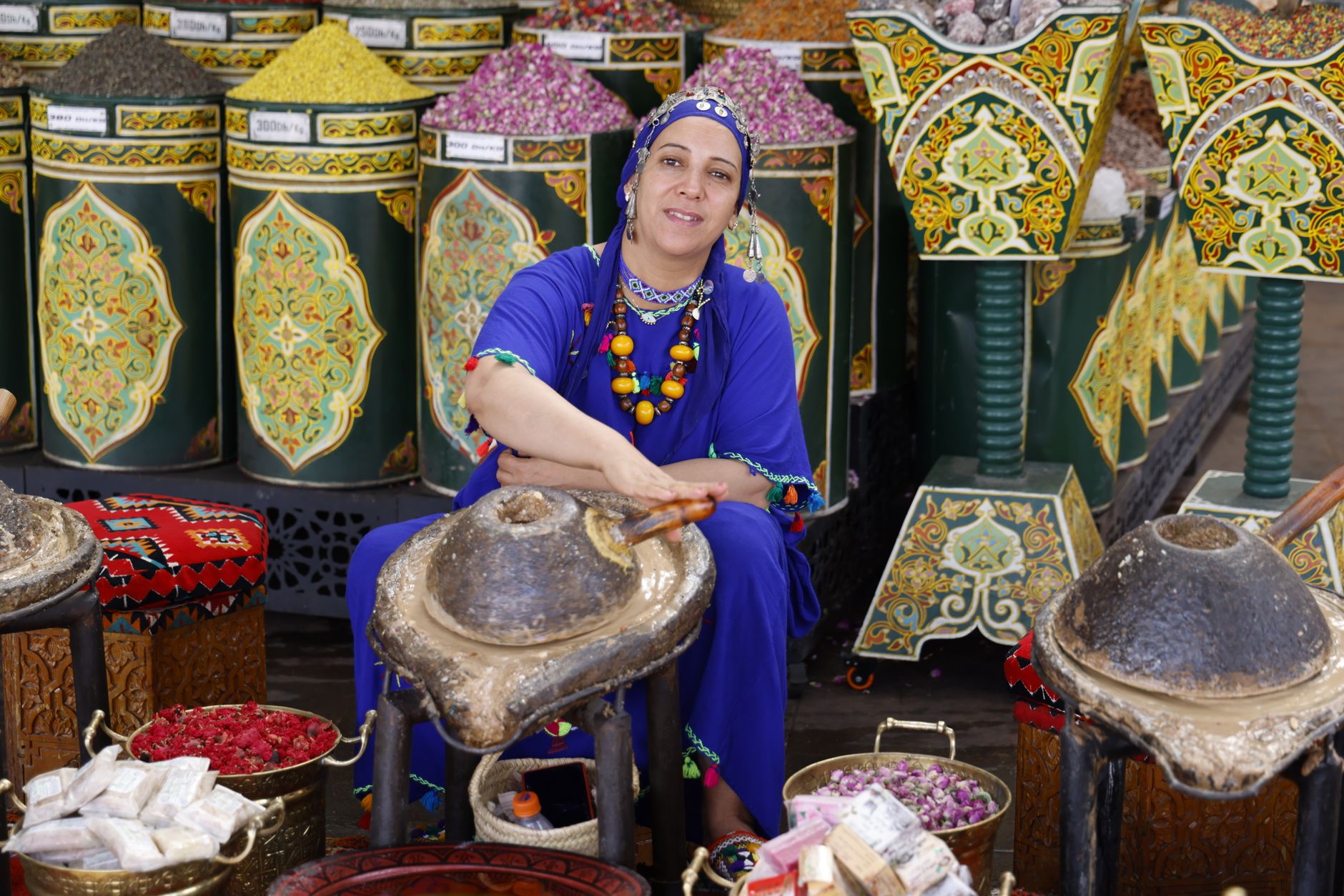 A bustling market square, Rahba Kedima, in Marrakech with stalls selling colorful spices, herbs, and traditional remedies under awnings.