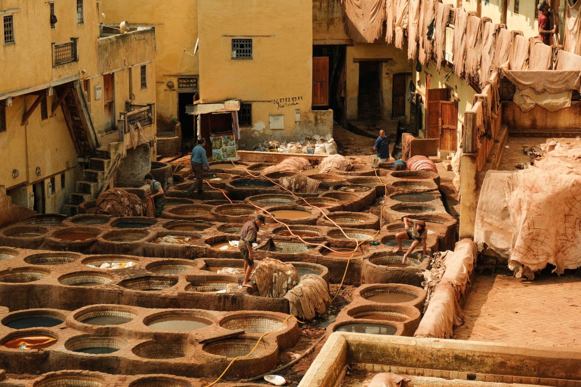 An artisan in a small workshop in Marrakech, working on a leather item with traditional tools, surrounded by raw materials and finished goods.