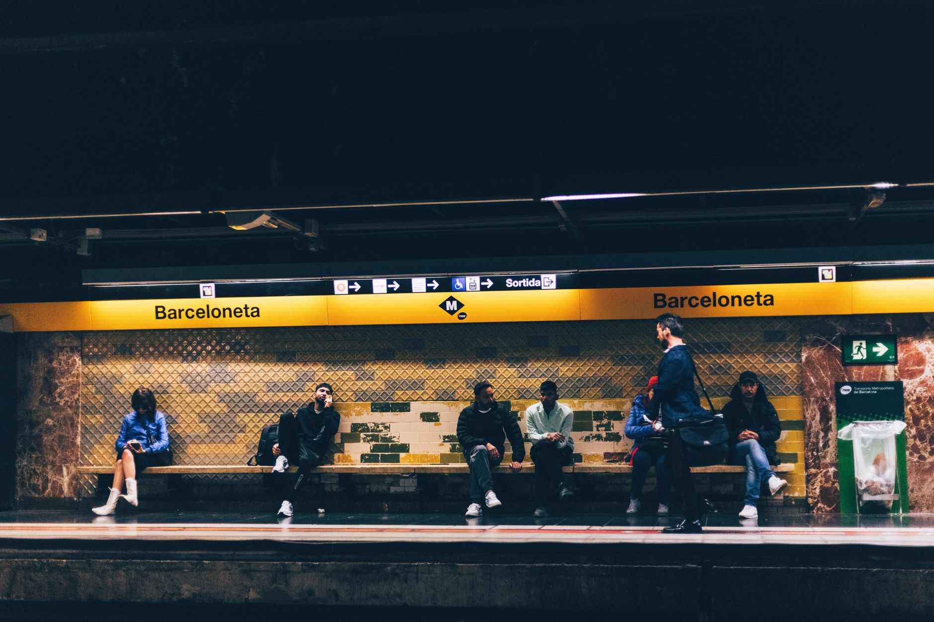 A clean, modern Barcelona metro station with a train arriving, showing clear signage and commuters waiting on the platform.