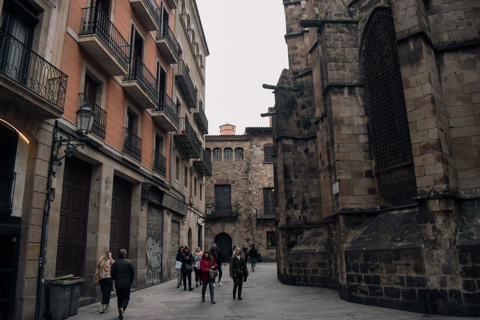 A narrow, ancient street in Barcelona's Gothic Quarter, with people walking and historic buildings on either side, suggesting a vibrant city setting.