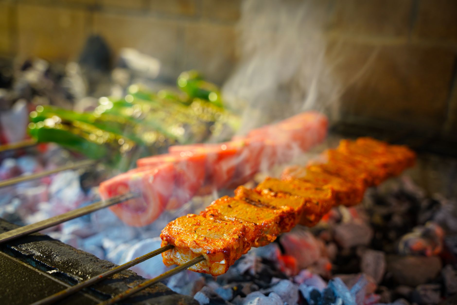 A chef grilling various types of Turkish kebabs over an open charcoal flame in a busy restaurant kitchen.