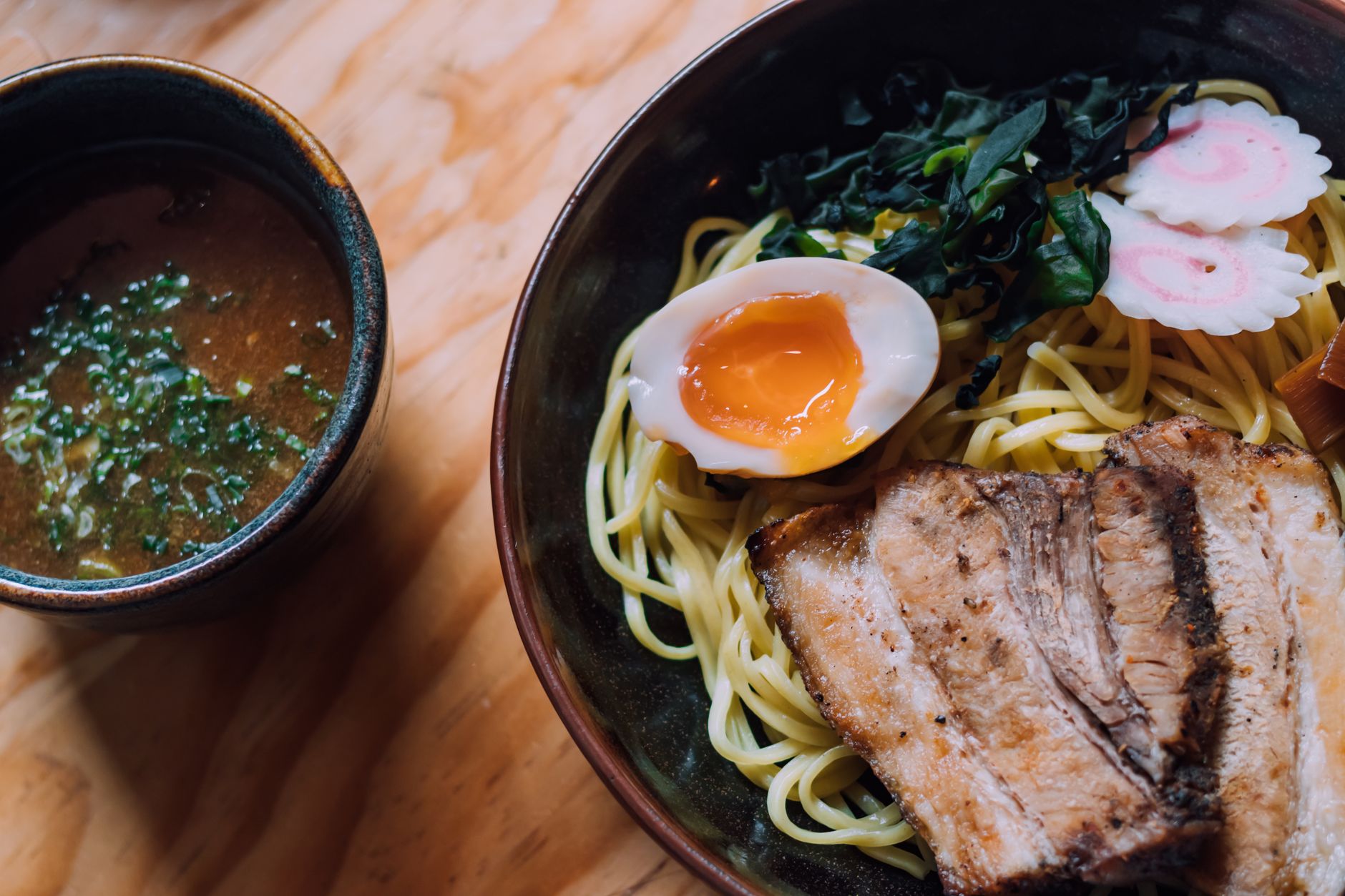 A bowl of thick tsukemen noodles next to a separate bowl of rich dipping broth with toppings.