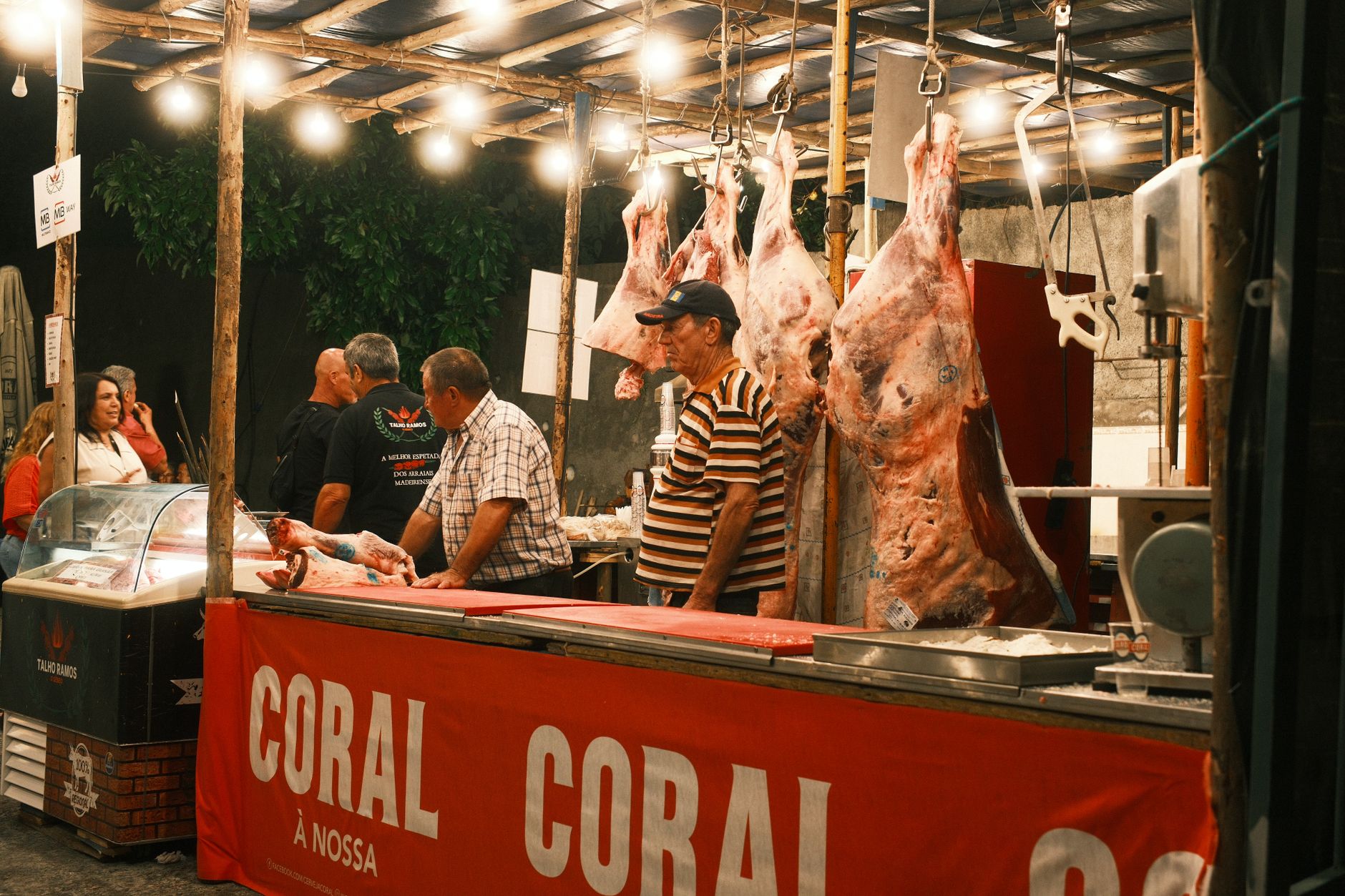 Large skewers of grilled beef espetada hanging vertically from a stand at a traditional Madeiran restaurant.