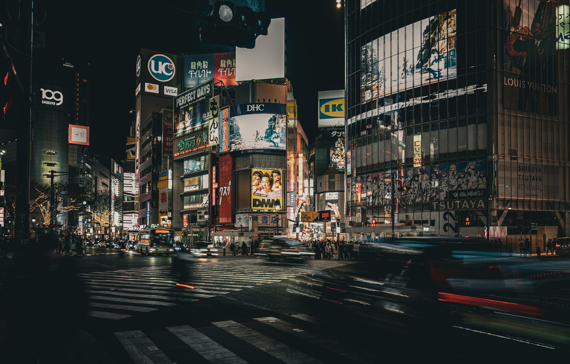 Thousands of pedestrians crossing the Shibuya Scramble intersection at night, surrounded by illuminated buildings and giant screens.
