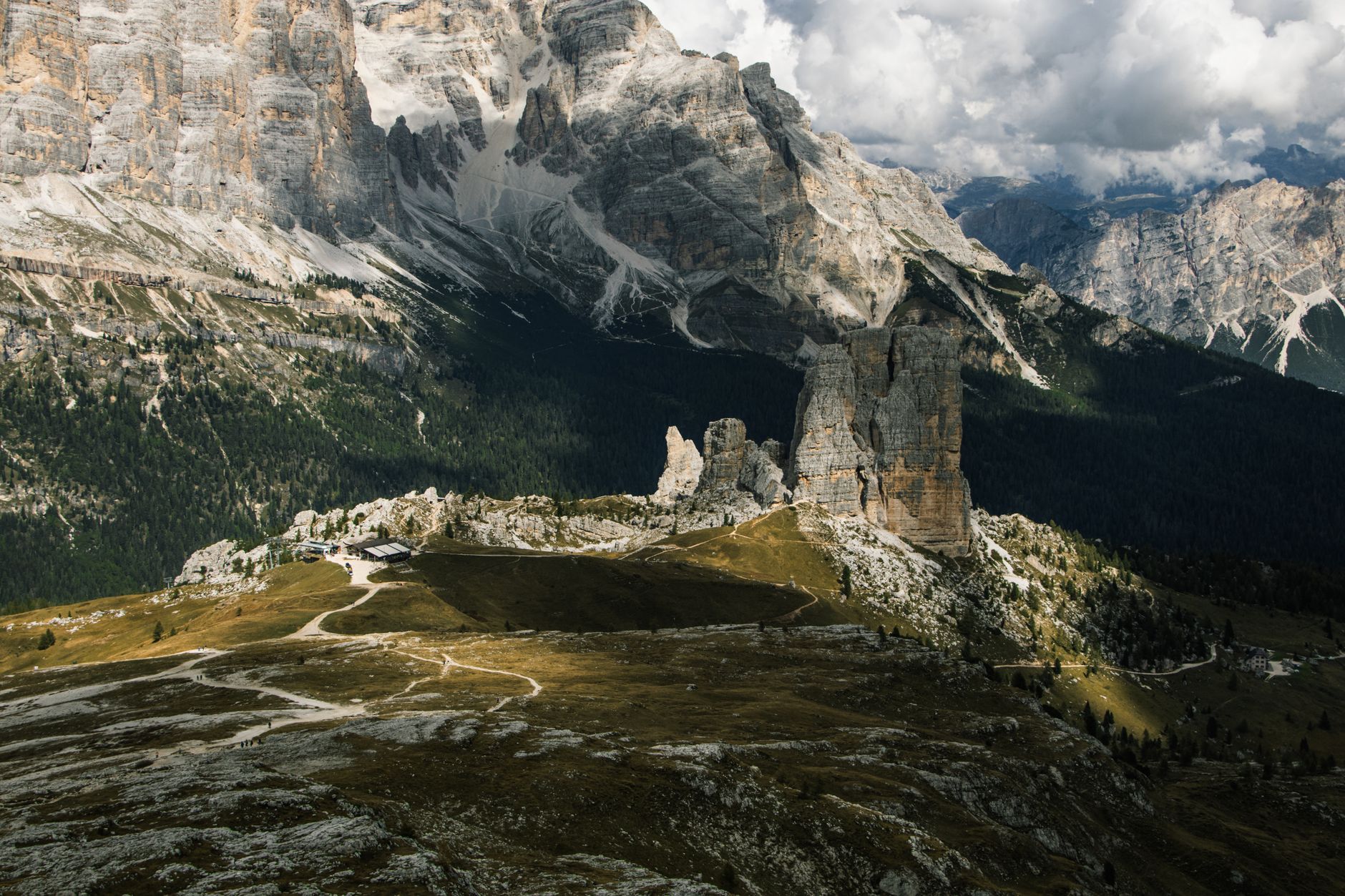 The distinct rock formations of Cinque Torri in the Dolomites, with a hiking trail and green landscape in the foreground.