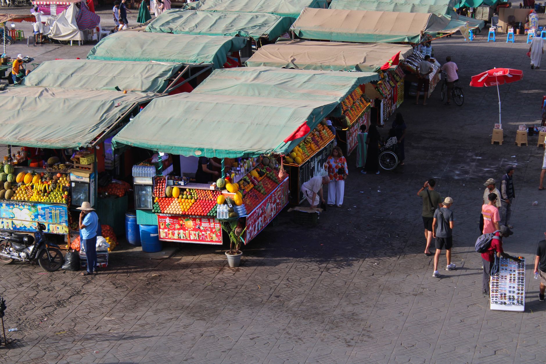 A vibrant, bustling scene in the Marrakech souks with colorful textiles, lamps, and people shopping, featuring a mix of shadows and bright light.