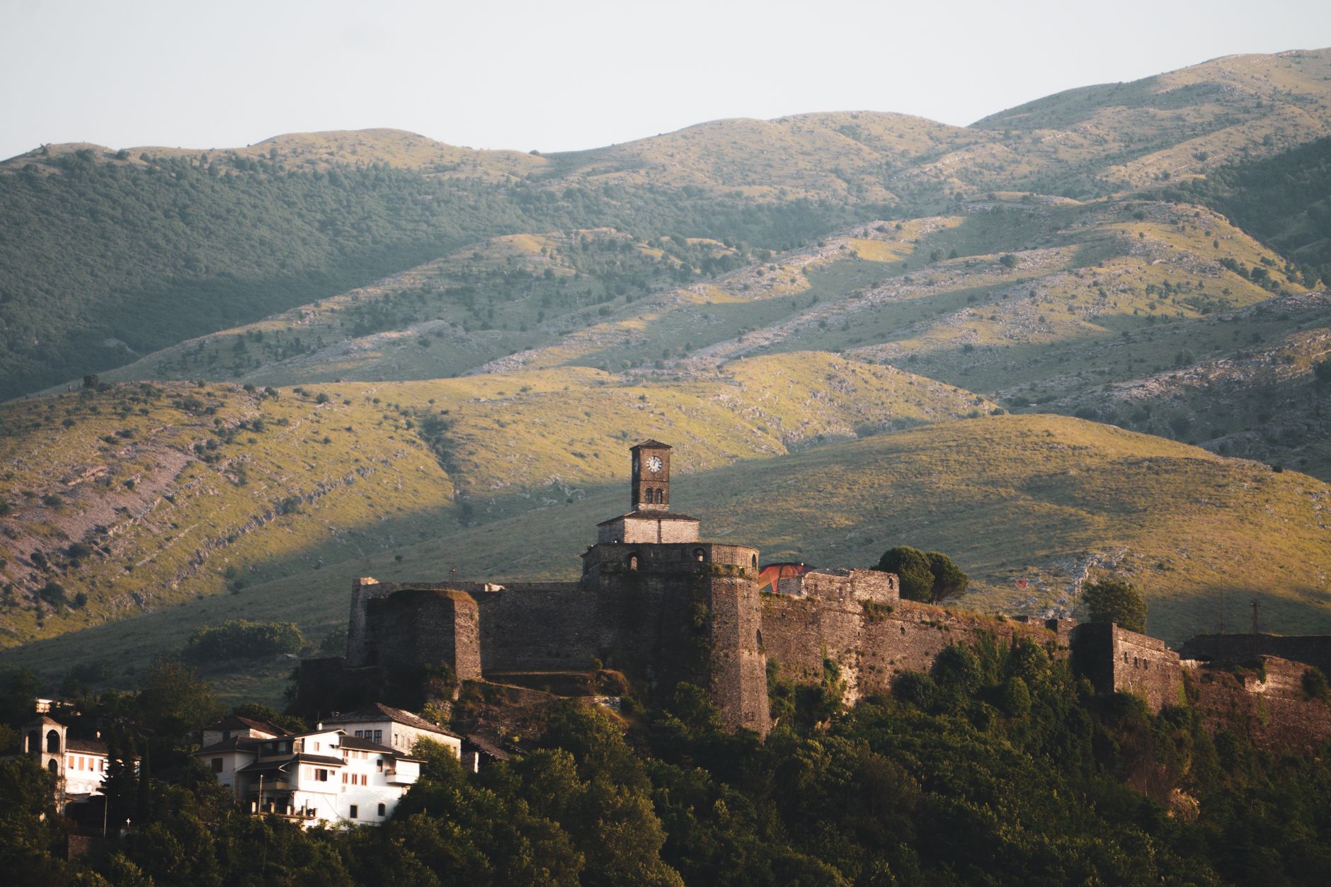 The historic stone city of Gjirokaster in Albania, with its distinct grey roofs and Ottoman architecture, built on a steep hillside with a large castle at the top.