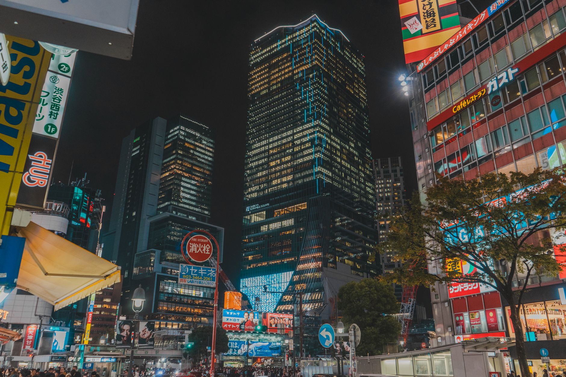 Bright neon signs illuminate the towering skyscrapers of Shinjuku at night, with people walking below.