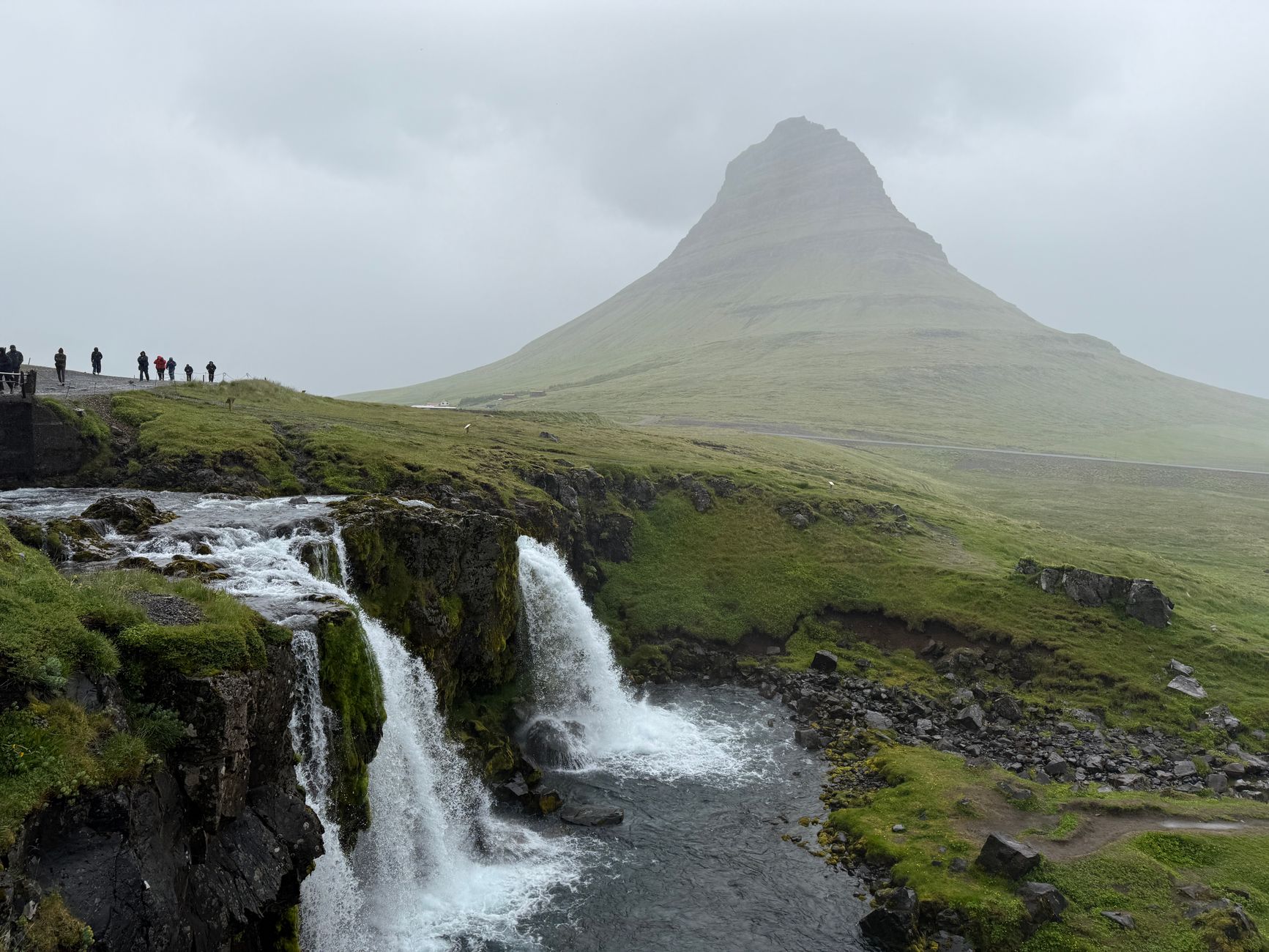 The iconic Kirkjufell mountain in Iceland, with its distinctive conical shape, reflected in still water under a cloudy sky.