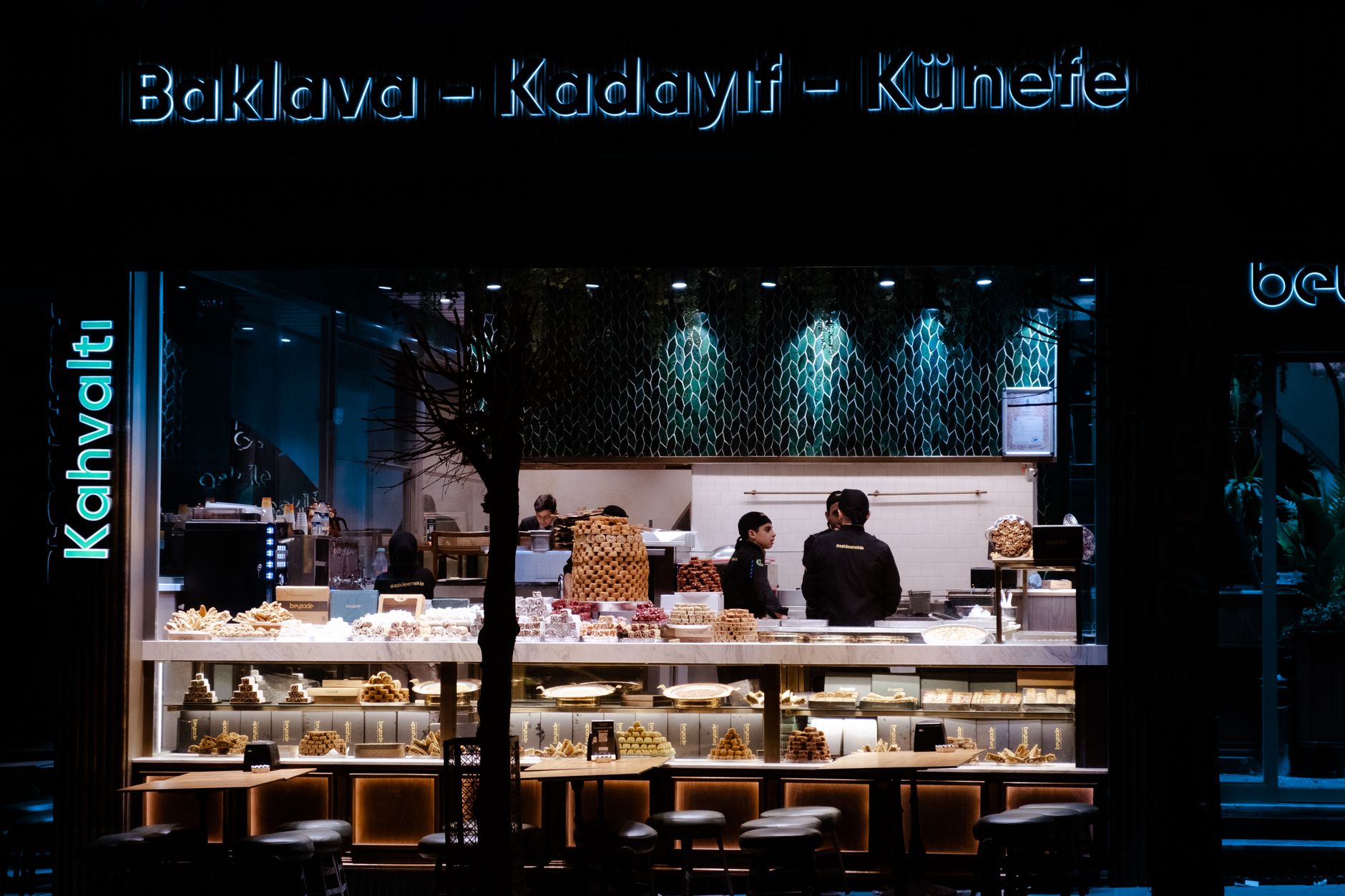 Inside a traditional baklava shop in Karakoy, Istanbul, with trays of glistening, freshly made baklava displayed under bright lights.
