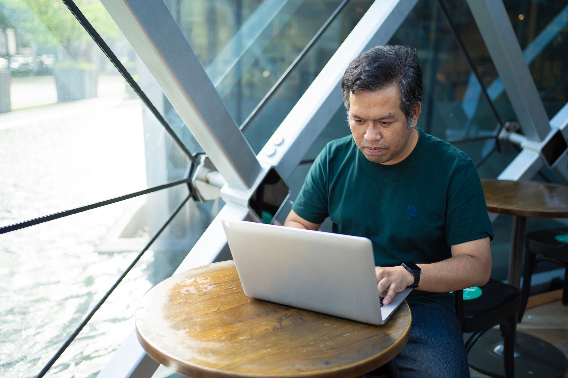 A person working on a laptop at a modern coworking cafe in Bangkok, with a smoothie and notebook on the table.