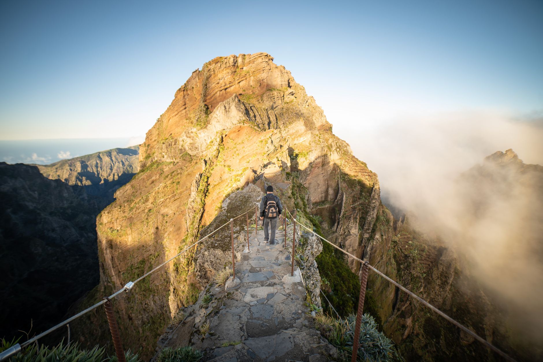 Sunlight illuminating jagged mountain peaks above a sea of clouds on the Pico do Arieiro to Pico Ruivo hike in Madeira.