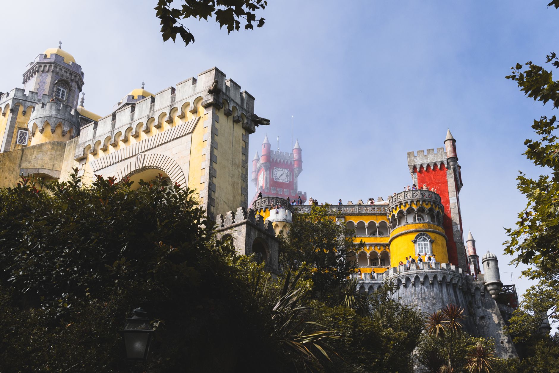 The vibrant yellow and red Pena Palace in Sintra, Portugal, with lush green trees and blue sky.