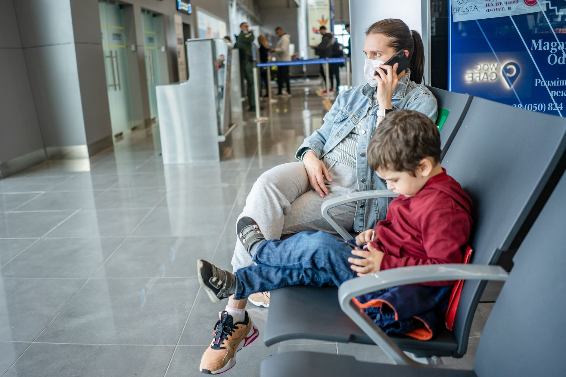 A person looking at their phone in an airport terminal, with luggage nearby.
