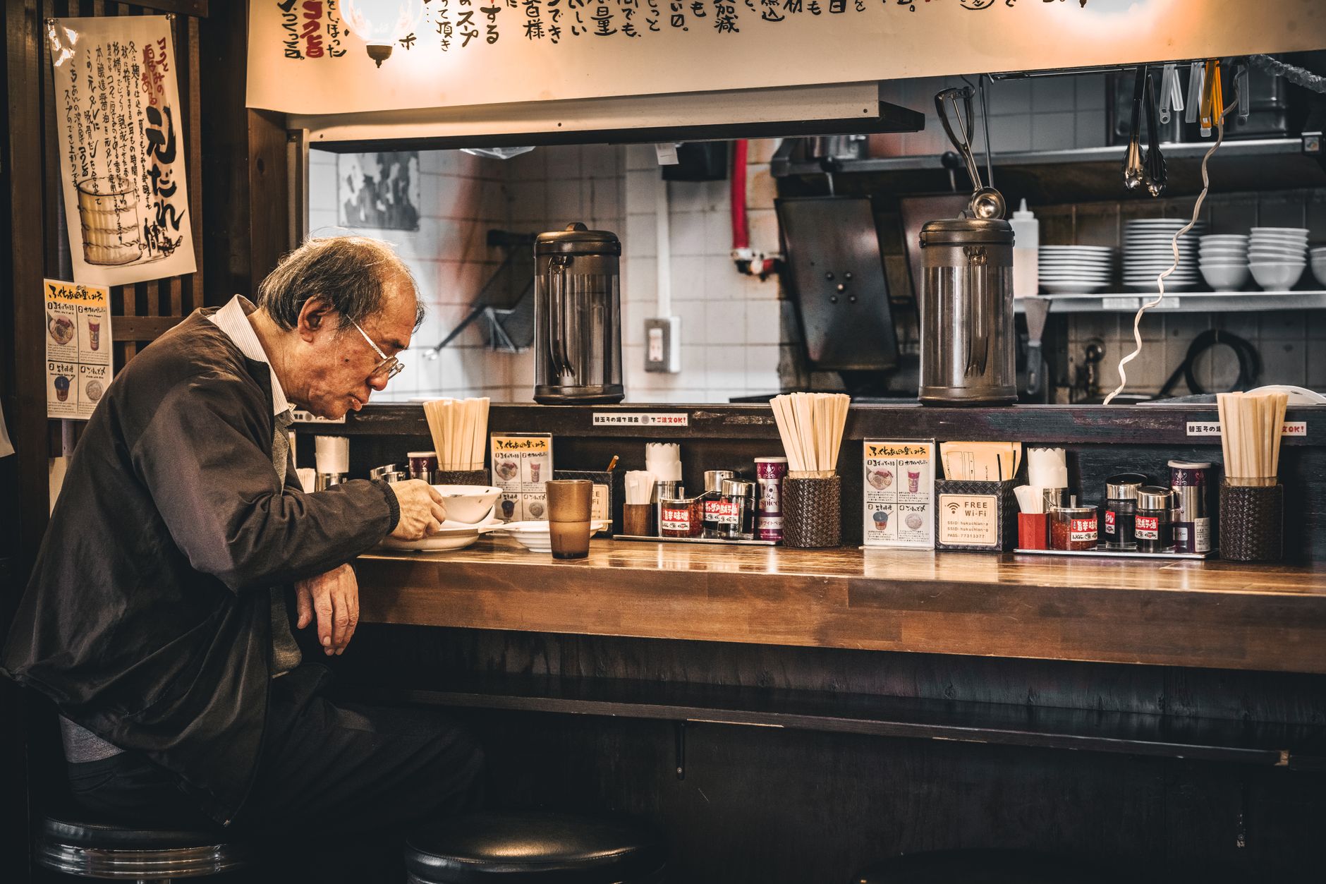 An inviting, brightly lit ramen shop interior in Tokyo with counter seating and steam rising from bowls.