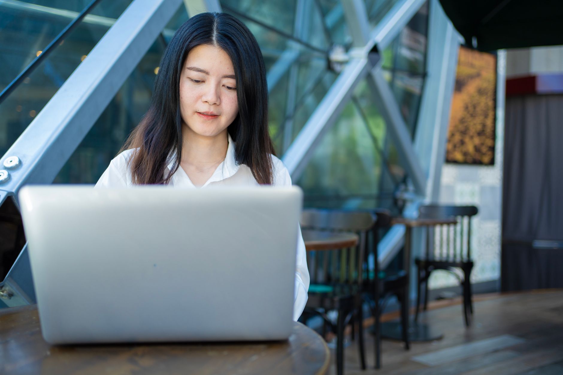 A woman working on a laptop in a bright cafe in Thailand, with tropical plants in the background.