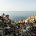 Turquoise water and sandy coastline of Amalfi Coast Italy with colorful beach umbrellas and cliffs in the background