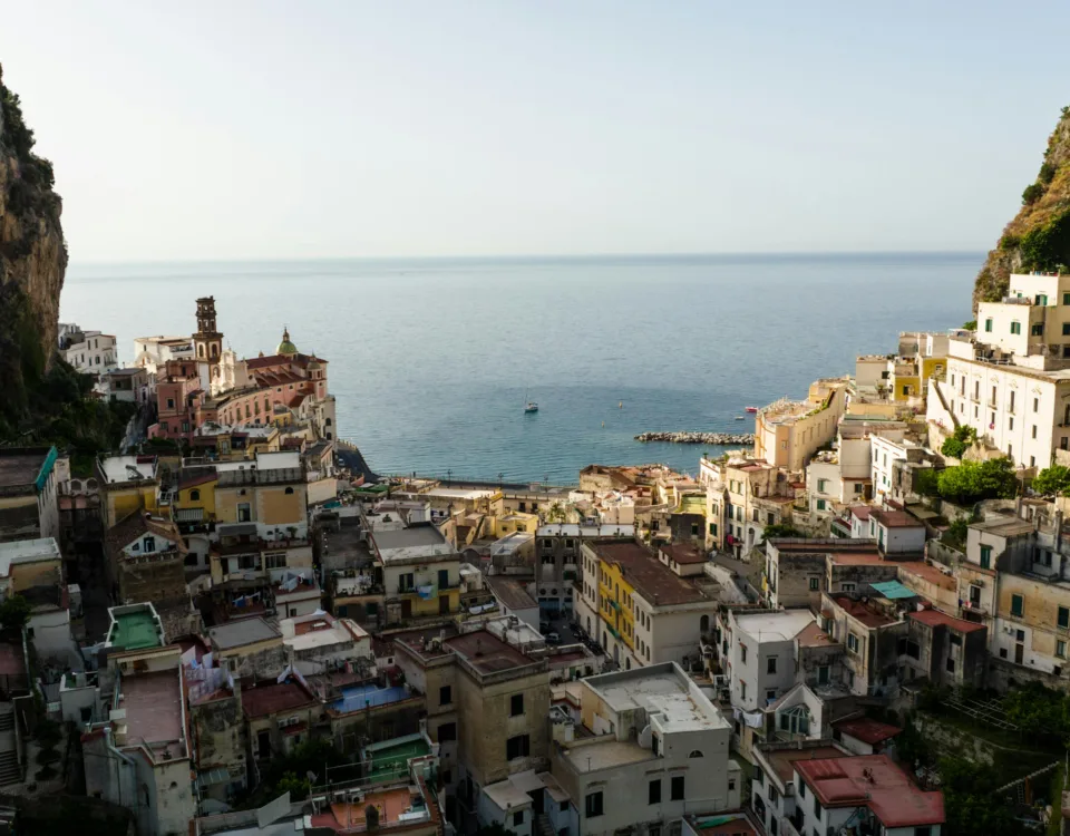 Turquoise water and sandy coastline of Amalfi Coast Italy with colorful beach umbrellas and cliffs in the background