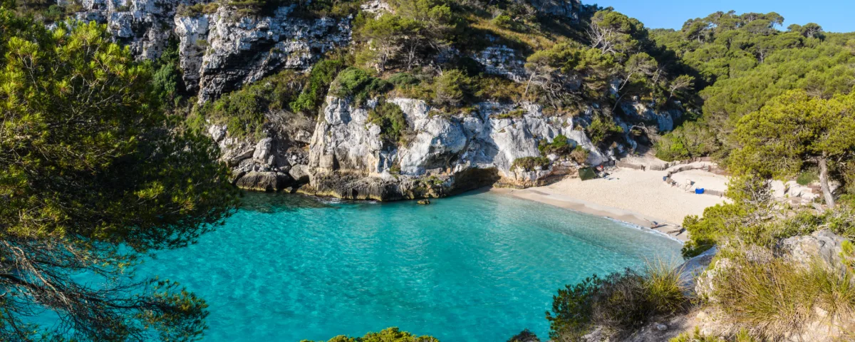 Sandy beach in Spain with clear blue water, sunbathers, and a scenic coastline under a bright sky
