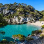 Sandy beach in Spain with clear blue water, sunbathers, and a scenic coastline under a bright sky