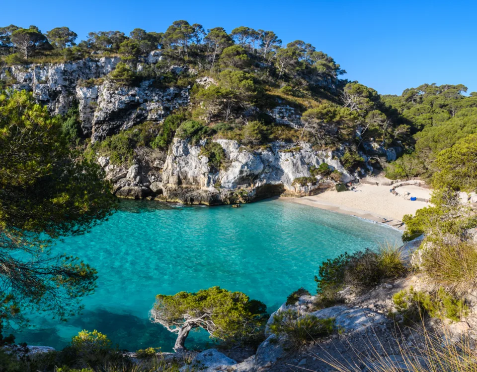 Sandy beach in Spain with clear blue water, sunbathers, and a scenic coastline under a bright sky