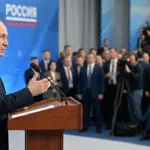 Russian President Vladimir Putin standing behind a wooden podium and speaking into microphones during a formal address.