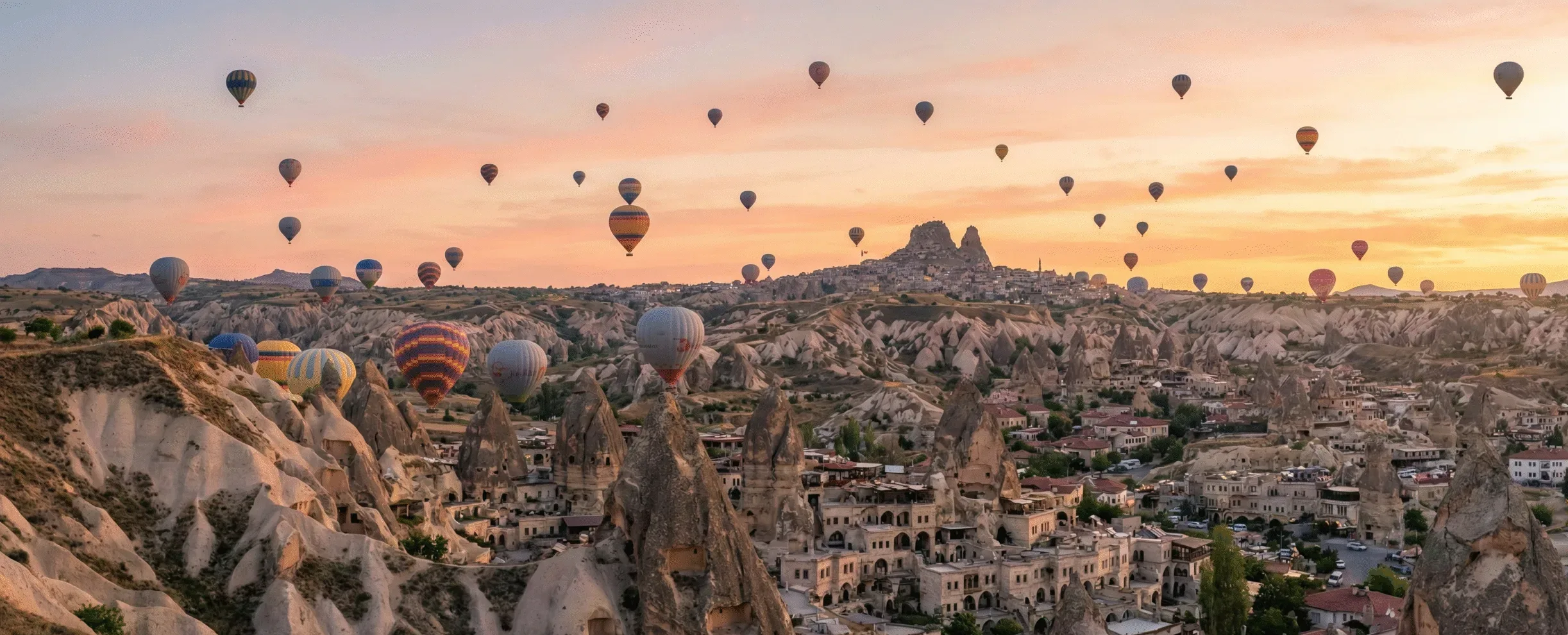 Breathtaking sunrise view of hot air balloons flying over the fairy chimneys of Göreme and Uçhisar Castle in Cappadocia, Turkey.