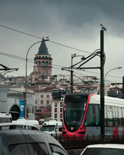 A public ferry crosses the Bosphorus in Istanbul, with a tram passing on the Galata Bridge and the city skyline behind.