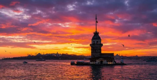 Dramatic sunset view of the Maiden's Tower (Kız Kulesi) from Üsküdar, with the historical peninsula of Istanbul in the background across the Bosphorus.
